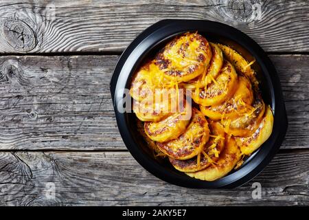 Hausgemachte Kartoffelkuchen mit geriebenem Cheddar-Käse in einem schwarzen Gericht auf einem rustikalen Holztisch, flach und frei Stockfoto