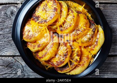 Hausgemachte Kartoffelkuchen mit geriebenem Cheddar-Käse in einem schwarzen Gericht auf einem rustikalen Holztisch, flach und nah Stockfoto