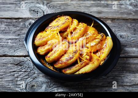 Hausgemachte Kartoffelkuchen mit geriebenem Cheddar-Käse in einem schwarzen Gericht auf einem rustikalen Holztisch aus nächster Nähe Stockfoto