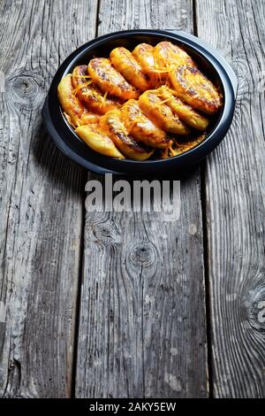 Hausgemachte Kartoffelkuchen mit geriebenem Cheddar-Käse in einem schwarzen Gericht auf einem rustikalen Holztisch, vertikaler Blick Stockfoto