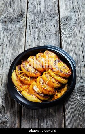 Nahaufnahme von hausgemachten Kartoffelkuchen mit geriebenem Cheddar-Käse in einem schwarzen Gericht auf einem rustikalen Holztisch, vertikale Ansicht Stockfoto