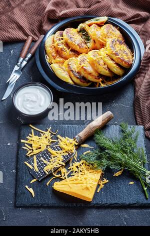 Hausgemachte Kartoffelkuchen mit Pilzen und Dillfüllungen mit geriebenem Cheddar-Käse in einem schwarzen Gericht auf einem Betontisch mit braunem Tuch Stockfoto