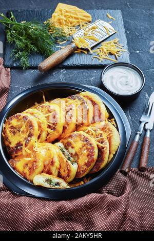Nahaufnahme hausgemachter Kartoffelkuchen mit Pilzen und Dillfüllungen mit geriebenem Cheddar-Käse in einem schwarzen Gericht auf einem Betontisch mit braunem c Stockfoto