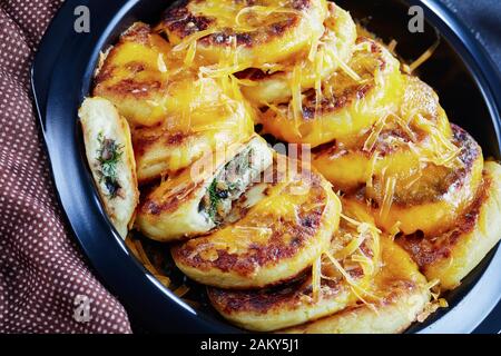 Nahaufnahme hausgemachter Kartoffelkuchen mit Pilzen und Dillfüllungen mit geriebenem Cheddar-Käse in einem schwarzen Gericht auf einem Betontisch mit braunem c Stockfoto