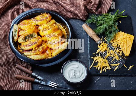 Nahaufnahme hausgemachter Kartoffelkuchen mit Pilzen und Dillfüllungen mit geriebenem Cheddar-Käse in einem schwarzen Gericht auf einem Betontisch mit braunem c Stockfoto