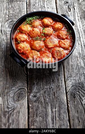 Bouletten de Poisson, gebratene Fischkugeln in Tomatensauce in einem schwarzen Gericht auf einem rustikalen Holztisch, vertikale Ansicht von oben Stockfoto