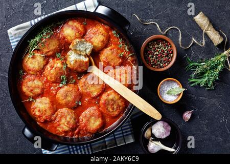 Bouletten de Poisson, gebratene Fischkugeln in Tomatensauce in einem schwarzen Gericht auf einem Betontisch mit Zutaten, horizontale Ansicht von oben, flacher Lay Stockfoto