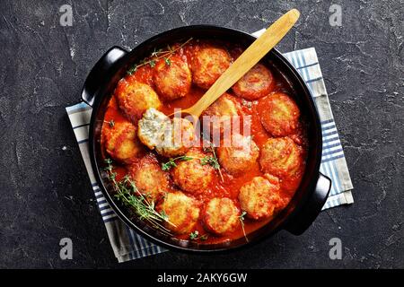 Nahaufnahme von Bouletten de Poisson, gebratene Fischkugeln in Tomatensauce in einem schwarzen Gericht auf einem Betontisch, horizontale Ansicht von oben, flacher Lay Stockfoto