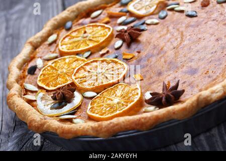 Nahaufnahme von Süßkartoffelkuchen mit orangefarbenen Pommes, Kürbiskernen und Anissternen auf einem rustikalen Holztisch, horizontaler Blick von oben, Stockfoto