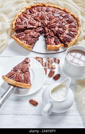Nahaufnahme der auf einer weißen Platte mit heißer Schokoladenmilch geschnittenen Pecan Pie, vertikale Ansicht von oben Stockfoto