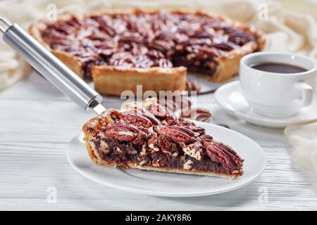 Nahaufnahme einer Scheibe köstlicher Pecan Pie. Kaffee in einer Tasse und geschnittener Pecan Pie im Hintergrund, Ansicht von oben, Makro Stockfoto