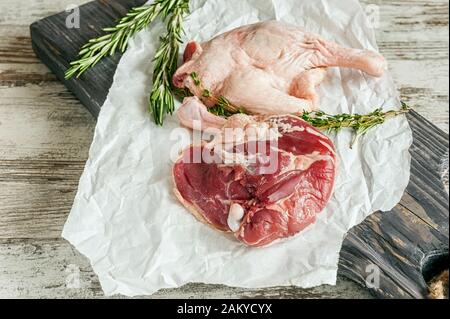 Rohe Entenschenkel. Das Geflügelfleisch ist bereit zum Kochen auf Papier und einem Holzschneidebrett. Stockfoto