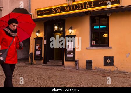 Eine rot gekleidete Frau mit rotem Regenschirm läuft an einem Restaurant in der Altstadt von Lublin, Polen, vorbei Stockfoto