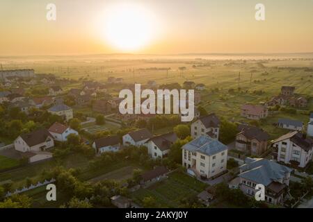 Luftaufnahme der ländlichen Wohngebiet mit privaten Häusern zwischen grünen Feldern bei Sonnenaufgang. Stockfoto