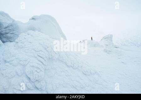 Schneeweiße Landschaft mit einem Kletterer in den Bergen. Malerischer Horstfrost auf Felsen im Nebel Stockfoto