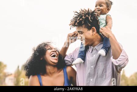 Glückliche afrikanische Familie hat Spaß im öffentlichen Park - Vater Mutter und kleine Tochter genießen Zeit und lachen zusammen - Konzept für Liebe und Elternschaft Stockfoto