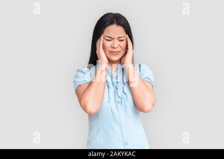 Freistil. Asiatische Frau, die isoliert auf Weiß steht und Kopfschmerzen hatte, irritiert Stockfoto
