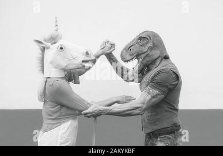 Verrücktes Paar tanzt und trägt Dinosaurier- und Einhorn-Maske - ältere Trend-Leute, die beim Karnevalszug maskiert Spaß haben Stockfoto