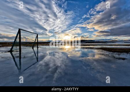 Sonnenuntergang über Wolken, Eisballspielplatz überflutet mit schmelzendem Schnee, Winter auf dem Bauernhof Moedrudalur auf der Straße vom See Myvatn nach Egilsstadir, Island Stockfoto