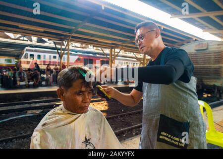 Bangkok/Thailand-Dezember 2019: Ein straßenbarber, der seinem männlichen Kunden auf einem Bahnsteig am Bahnhof Hua Lamphong kostenlose Frisur gibt. Stockfoto