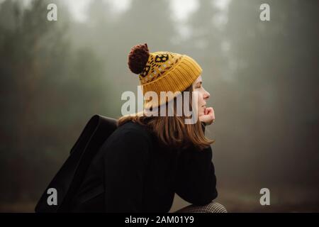 Nachdenkliche Frau sitzt am Wald bei nebligen Wetter Stockfoto