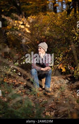 Teen junge sitzt allein auf Log in Wald Blick aus nachdenklich. Stockfoto
