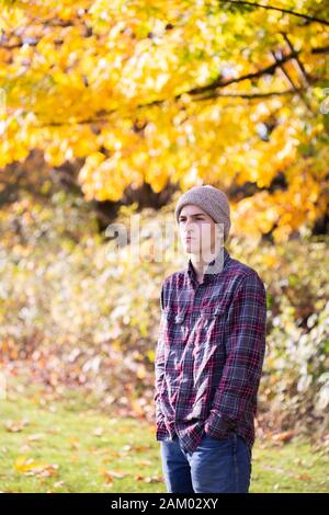 Nachdenklicher Teenager-Junge in Haube und Flanell-Hemd vor gelben Bäumen Stockfoto