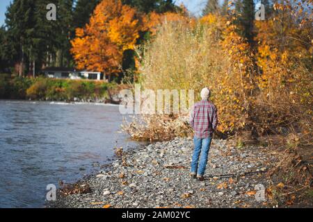 Teenager-Jungen in Jeans, kariertes Hemd und Beanie Spaziergänge entlang Fluss im Herbst. Stockfoto