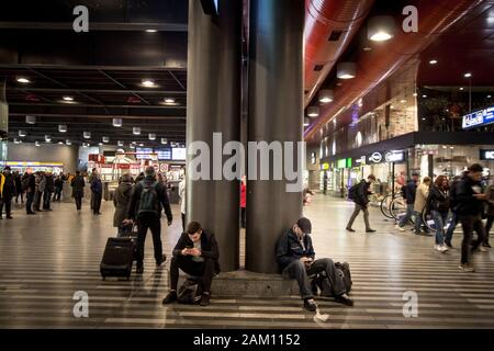 Prag, TSCHECHIEN - 31. OKTOBER 2019: Zwei junge Männer, Pendler, sitzend und mit ihren Smartphones unterwegs in der Abflughalle Stockfoto