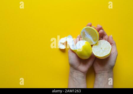 Blick von oben auf die weibliche Hände, die ganze und aufgeschnittene reife Zitronen auf gelbem Untergrund, Konzept der Gesundheit und Vitamine Stockfoto