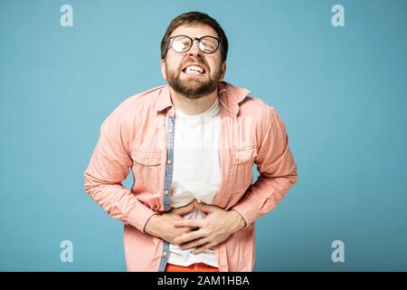 Der Mensch leidet unter sehr starken Schmerzen in der Bauchhöhle, grinst und schließt die Augen ab. Stockfoto