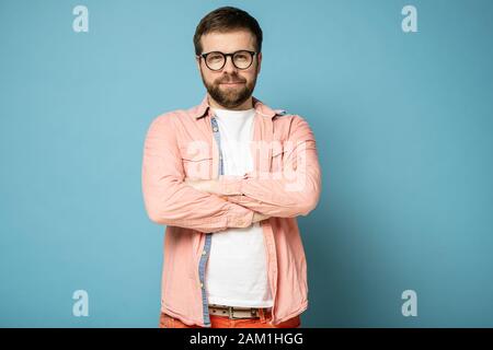 Gutmütiger bärtiger Mann mit Brille steht selbstbewusst mit gekreuzten Armen und starrt intensiv an die Kamera. Stockfoto