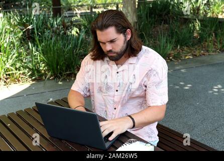 Winkel eines bärtigen Mann in seiner Jugend, dass Studieren auf seinem Laptop im Park außerhalb an einem warmen Sommertag ist. Stockfoto