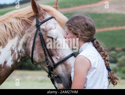 Mädchen, die vor ihrem Sabino-Malpferd stehen, das sich gegenübersteht und das Pferd auf der Stirn küsst. Stockfoto