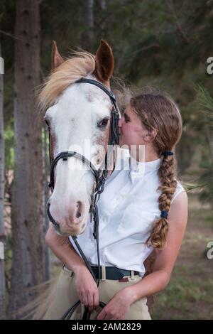 Das Mädchen, das neben ihrem Sabino-Malpferd steht, zeigt beide in der Nähe der Kamera des Mädchens, das das Pferd küsst. Stockfoto