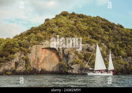 Taupo, North Island, Neuseeland - 26. Dezember 2016: Touristen, die sich mit einem Kreuzfahrtschiff den berühmten Schnitzereien Des Mine Bay Maori Rock am Lake Taupo nähern Stockfoto