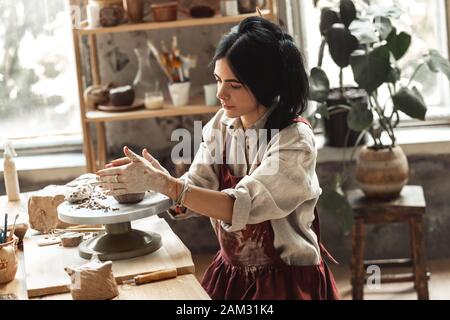 Craftsperson Konzept. Junge Frau, die am Tisch sitzt und Keramik in Innenräumen rollenden Ton macht, der sich konzentriert Stockfoto