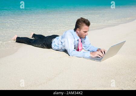 Entspannt Geschäftsmanns, der auf seinem Laptop liegen im Freien am Ufer eines hellen tropischen Strand Stockfoto