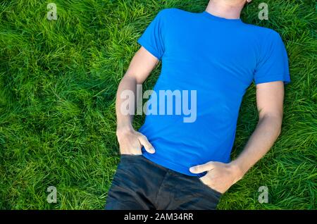 Nicht wiederzuerkennen, junger Mann im blauen T-Shirt mit Kopie Raum liegen im Freien in einem Patch von üppigen grünen Rasen Stockfoto