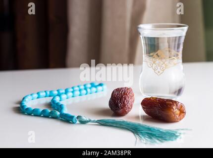 Zwei frische Datteln Medjool, Glas Wasser und Rosenkranz auf weißen Tisch. Stockfoto