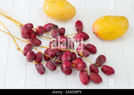 Zwei rohe reife Mango- und Bunchzweige frische Datteln weißer Holzhintergrund Top View Stockfoto