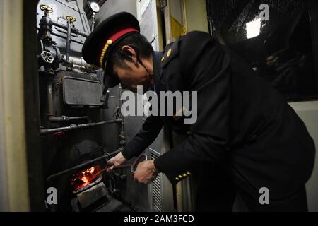 (200111) - LANZHOU, Jan. 11, 2020 (Xinhua) - zugbegleiter Zhang Guoxing bringt Kohle in den Kessel für die Heizung im Zug Nr. 7505 im Nordwesten der chinesischen Provinz Gansu am Jan. 10, 2020. Der Zug Nr. 7505, die reist von Lanzhou, Wuwei, ist ein vier-Schlitten gewöhnlicher Zug. Der Zug, der mehr als ein Dutzend kleine Stationen zwischen Lanzhou und Wuwei, läuft 290 Kilometer in 5 Stunden und 27 Minuten. Der volle Fahrpreis beträgt 18,5 Yuan (etwa 2,7 US-Dollar), mit den niedrigsten Tarif von 1 Yuan. Es läuft seit fast 40 Jahren seit den 1980er Jahren, mit fast 10 Millionen Passagiere. Dur Stockfoto