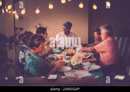 Fröhliche und freundliche Menschen, die zu Hause oder im Restaurant zusammen zu Abend essen, in Freundschaft - Familie mit verschiedenen Alters und Generationen Männer und Frauen genießen Stockfoto