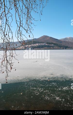 Winterlandschaft mit gefrorenem See und einigen Baumzweigen als Rahmen am See Orestiada in Kastoria, Griechenland Stockfoto