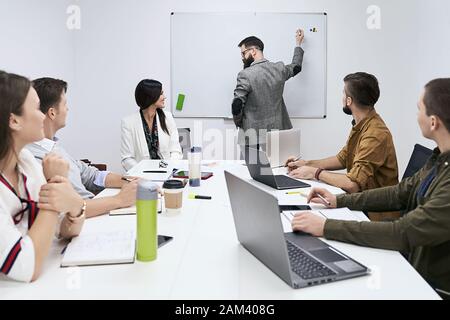 Der männliche Business Coach Speaker im Anzug präsentiert Whiteboard, Referentin Moderatorin Consulting Training überzeugt Mitarbeiter Kundengruppe, Mentor Stockfoto