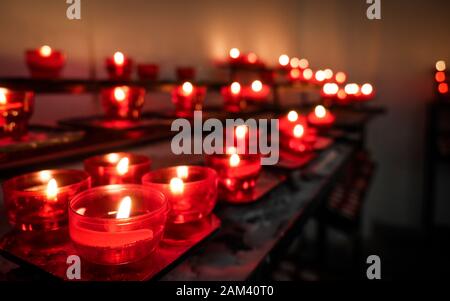 Kirchenaltar Votivkerzen. Flacher Fokus auf die Vordergrund-Gebetskerze mit Hintergrund-Kopierraum und Bokeh. Stockfoto