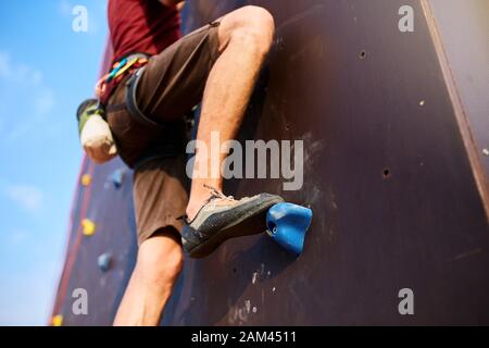 Unten Nahansicht des Felskletterfußes beim Training einer künstlichen Kletterwand im Freien. Man füße sich in Kletterschuhen auf Felsen mit Ausrüstung - hinausgezögert Stockfoto