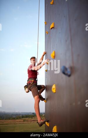 Sportlicher Mann beim Klettern im Fitnessstudio an der Trainingswand des Kunsteises im Freien. Junger abgeschwächter Kletterer beim Workout. Stockfoto
