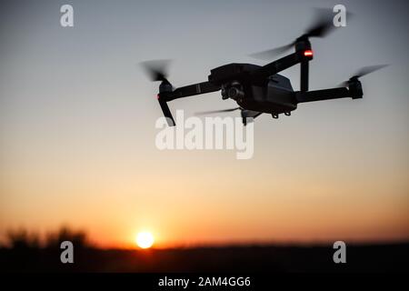 Kleiner kompakter Quadcopter fliegt bei Sonnenuntergang in der Luft. Drohne schwebt und bleibt stabil. Stockfoto