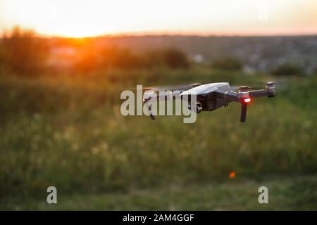 Kleiner kompakter Quadcopter fliegt bei Sonnenuntergang in der Luft. Drohne schwebt und bleibt stabil. Stockfoto